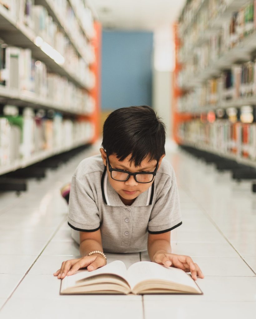 Smart school boy reading a book at the library